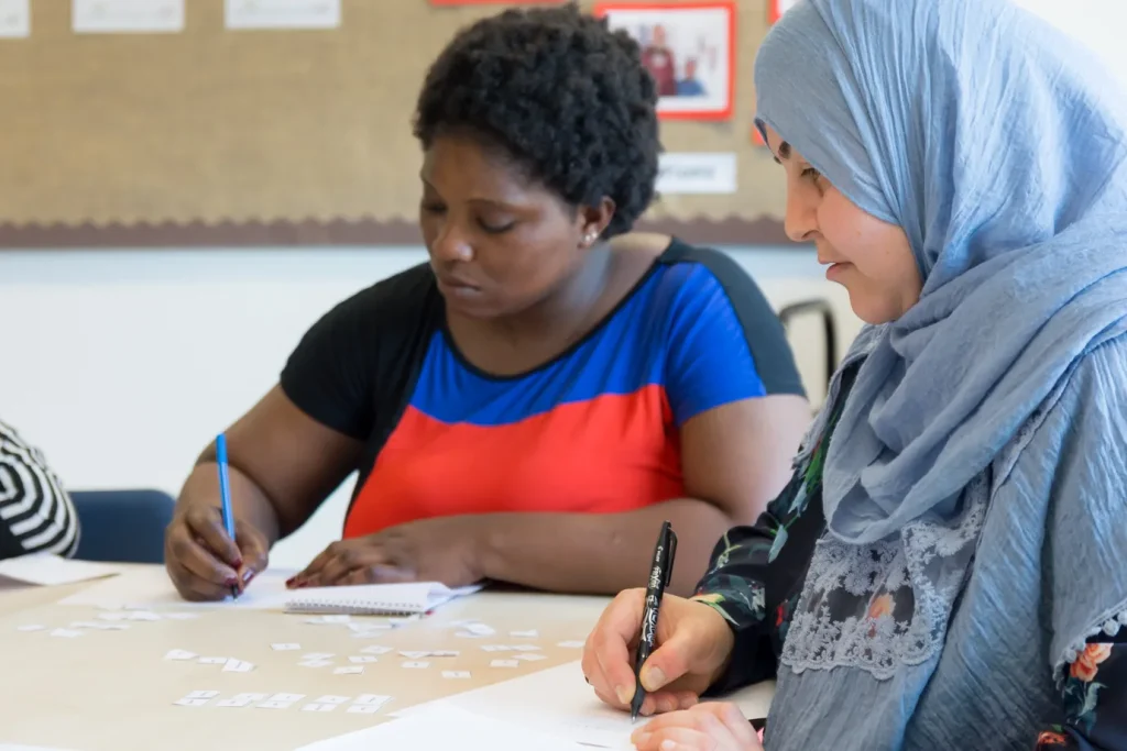 Two ESOL students writing exercises side by side, one wearing a hijab