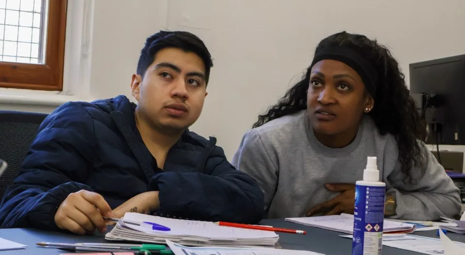 Two young adult learners sitting side by side in a classroom, listening attentively during a session