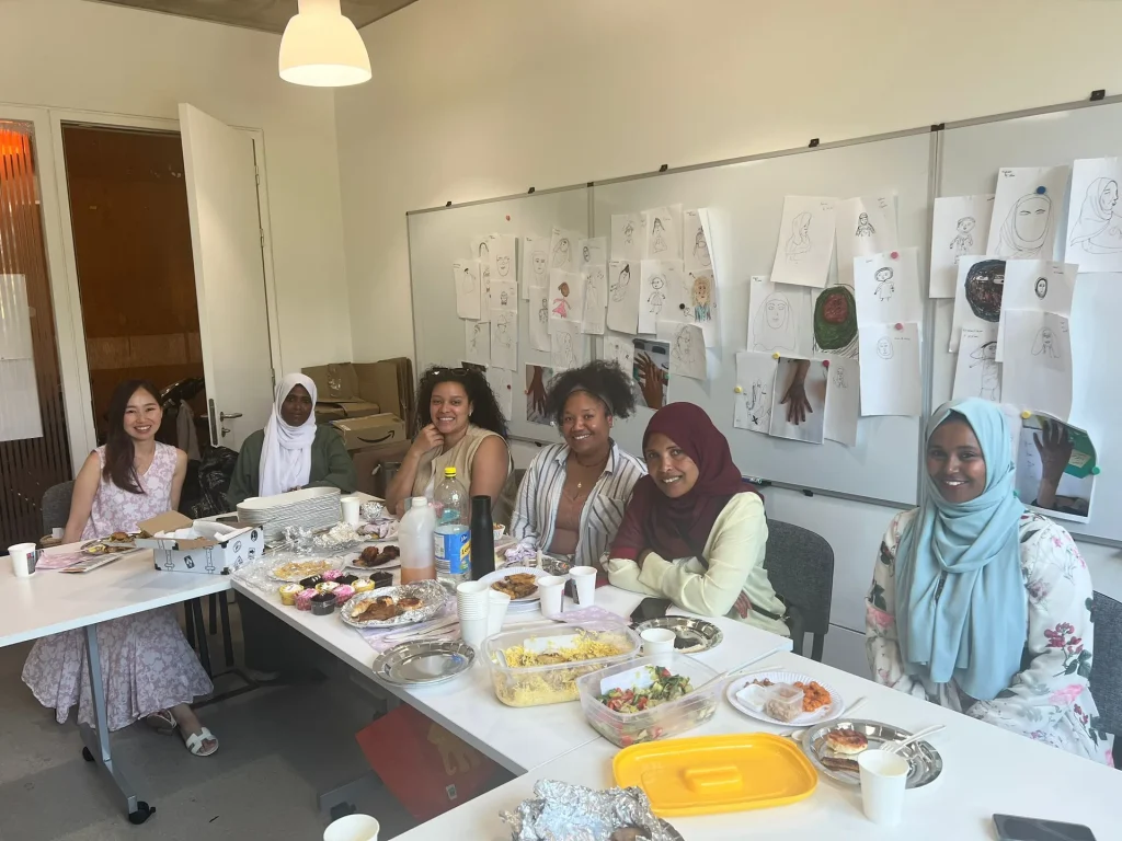 Group of women learners sharing food at a long table with artwork on the wall
