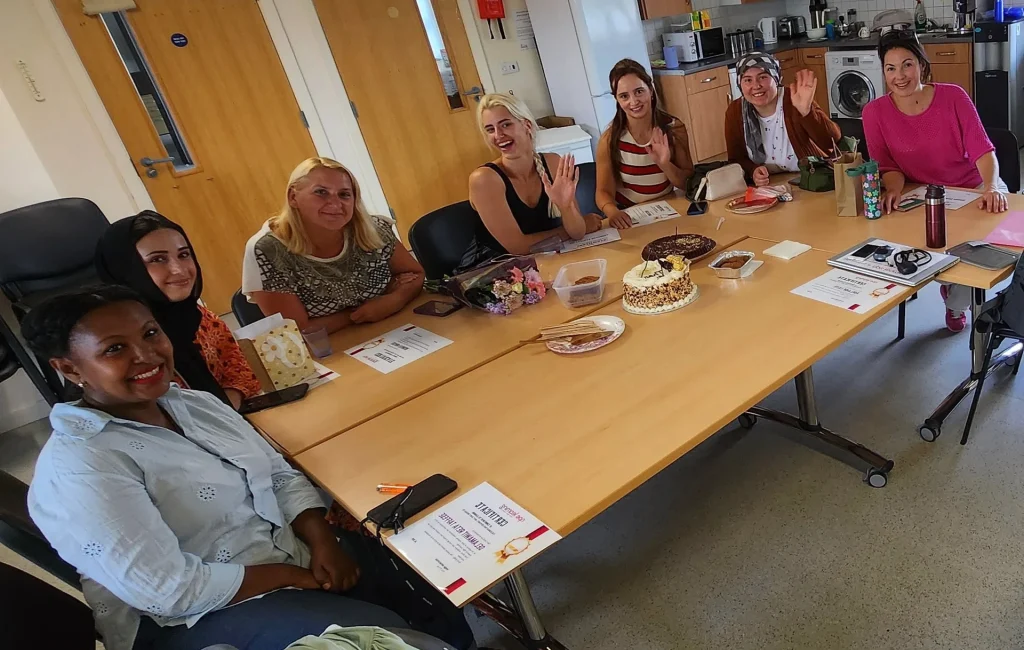 Group of learners around a table waving and smiling during a community lunch