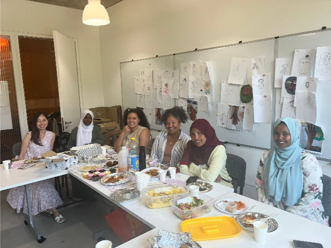 A group of women learners smiling together at a shared lunch in the classroom
