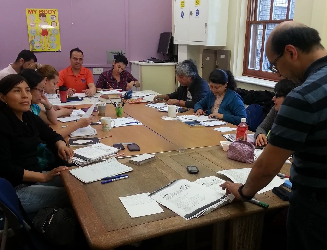 Adult learners working through English worksheets around a table with their tutor