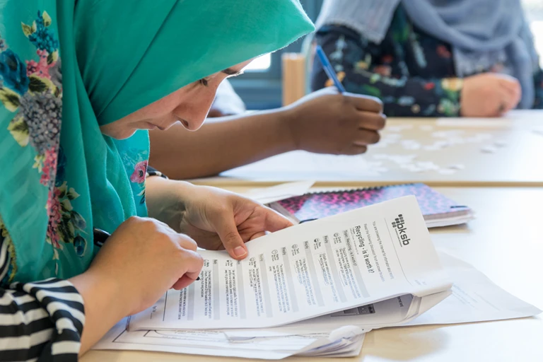 An adult learner in a green headscarf reading through a Functional Skills English worksheet in class